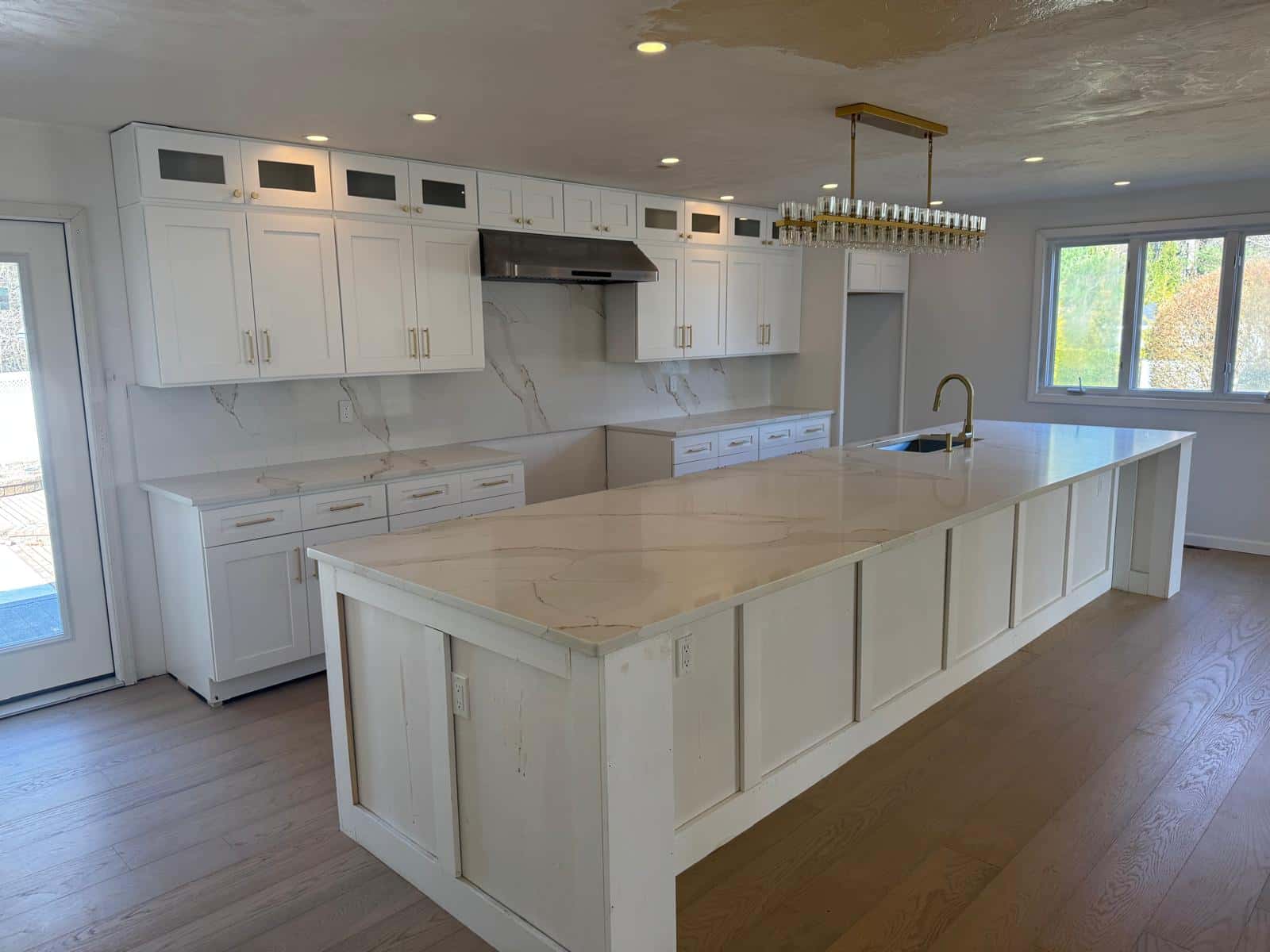 White kitchen with custom cabinetry, a long marble island and a brass chandelier